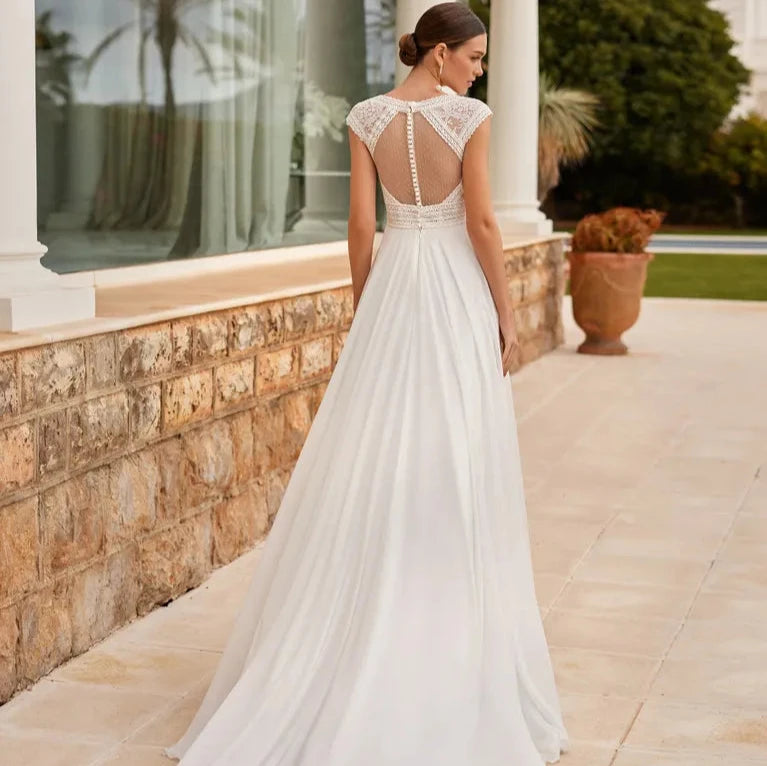 Robe de mariée bohème dos nu avec dentelle délicate et jupe fluide, portée par un mannequin sur fond neutre.