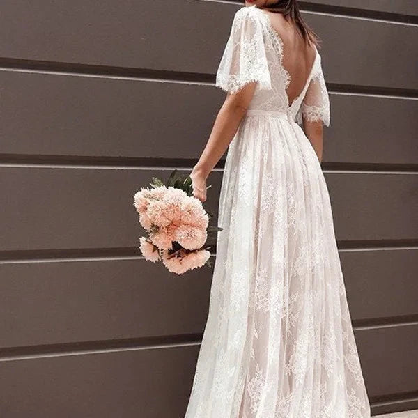 Robe de mariée bohème Paris, longue, en dentelle blanche avec détails floraux, portée par une mariée dans un champ.